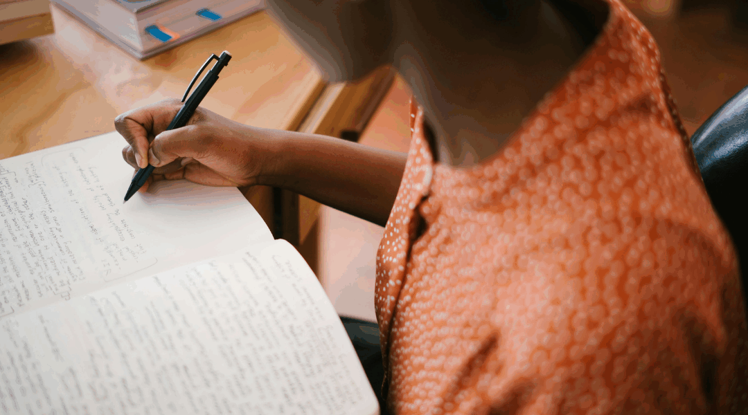 A woman sitting at her desk and writing in a notebook, representing everyday ways to apply your strengths at work.